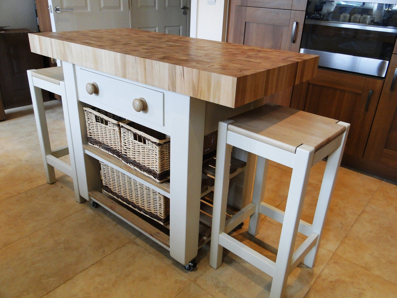 Kitchen island with wooden top and white base, accompanied by stools.