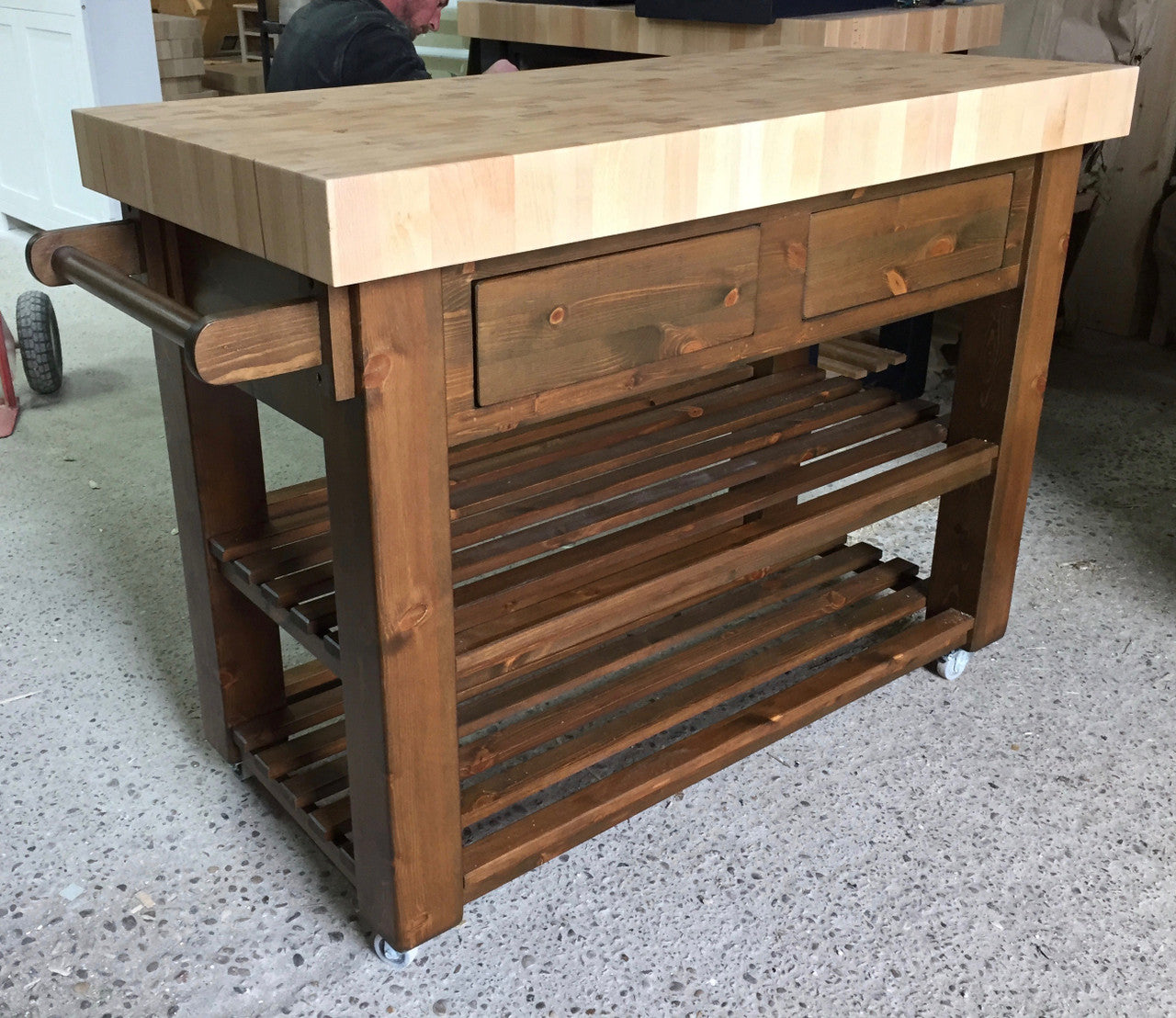 Wooden kitchen island with drawers and shelves on a concrete floor.