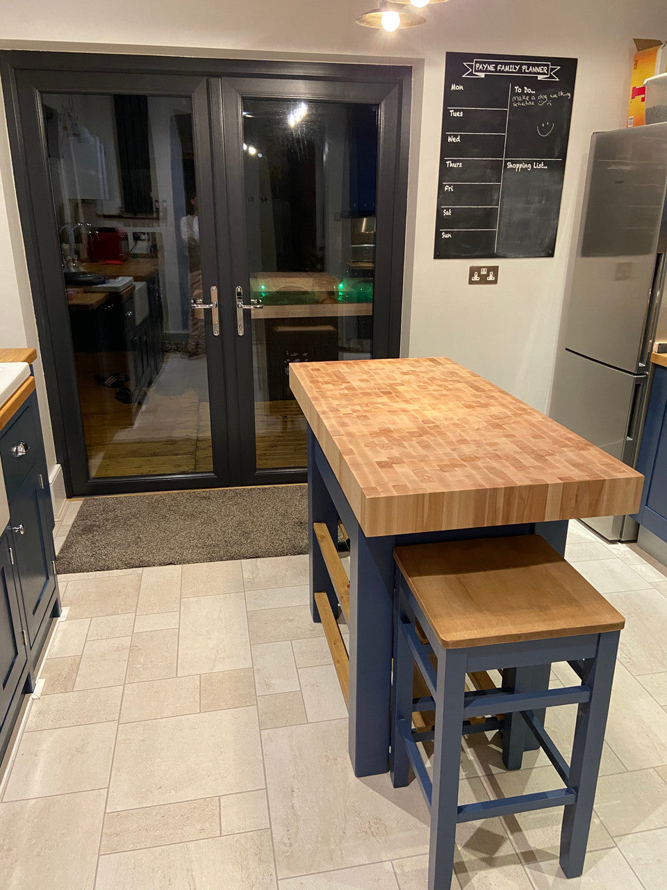Kitchen area with a wooden table and stools, refrigerator, and chalkboard on the wall.