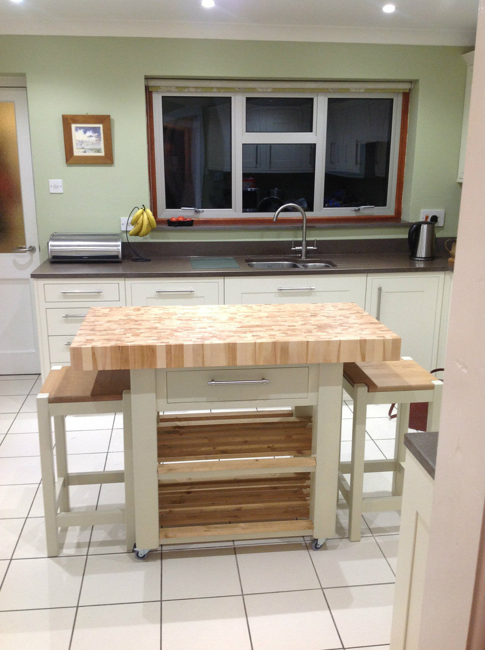 Kitchen with wooden island and stools, featuring a sink and window.
